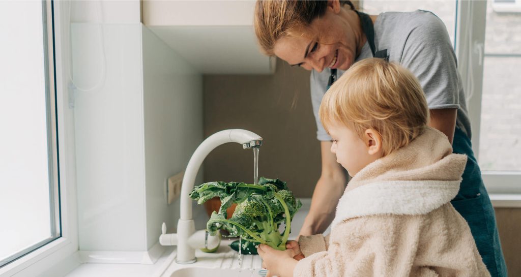 Madre y niño lavando brócoli con agua limpia del grifo en cocina, agua filtrada para el hogar Tuawa