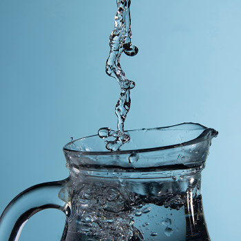 Agua vertiéndose en jarra de cristal con burbujas sobre fondo azul claro
