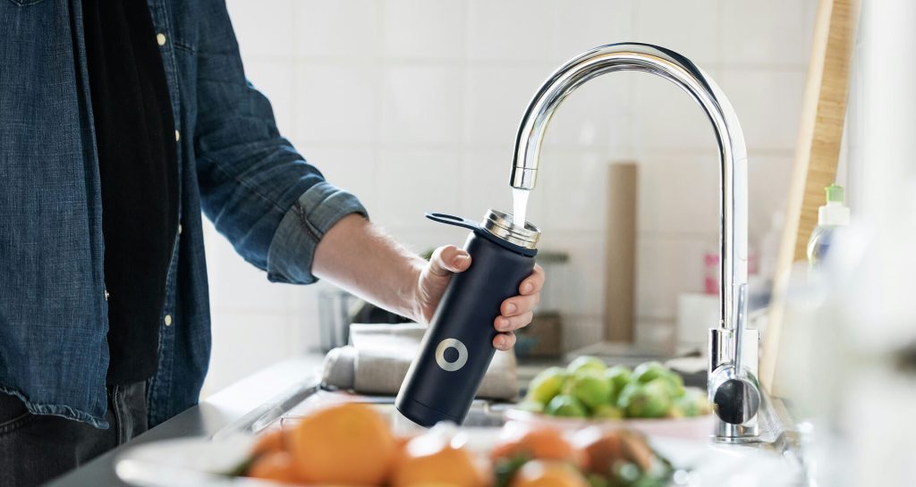 Persona llenando botella reutilizable con agua del grifo filtrada en cocina doméstica