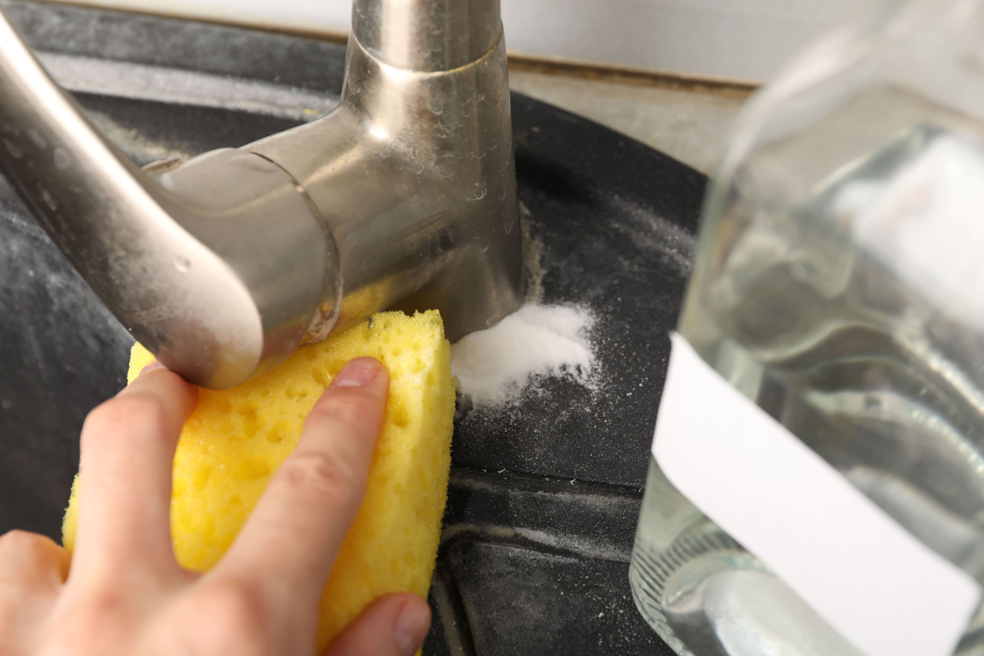 Mujer limpiando el grifo del fregadero con bicarbonato de sodio en la cocina, primer plano.